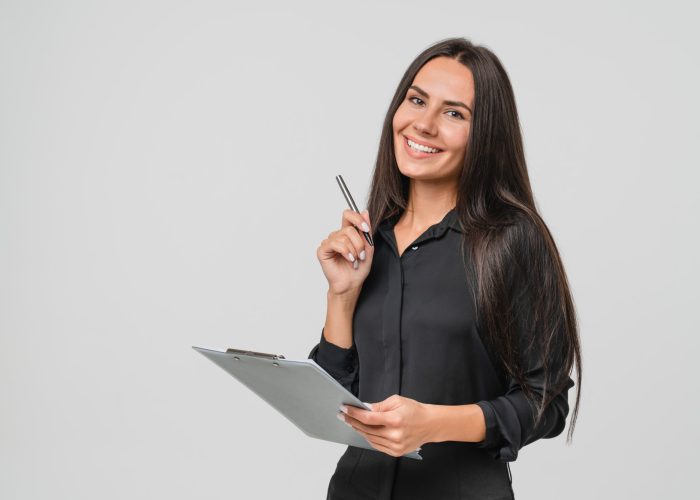 Smiling confident caucasian young businesswoman auditor writing on clipboard, signing contract document isolated in white background